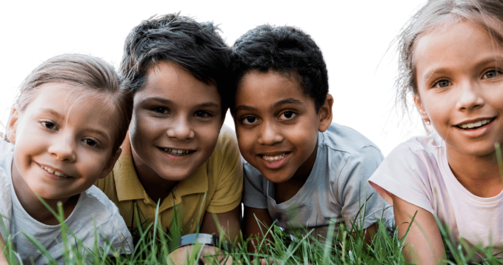 Four children smiling at the camera laying on a patch of grass.