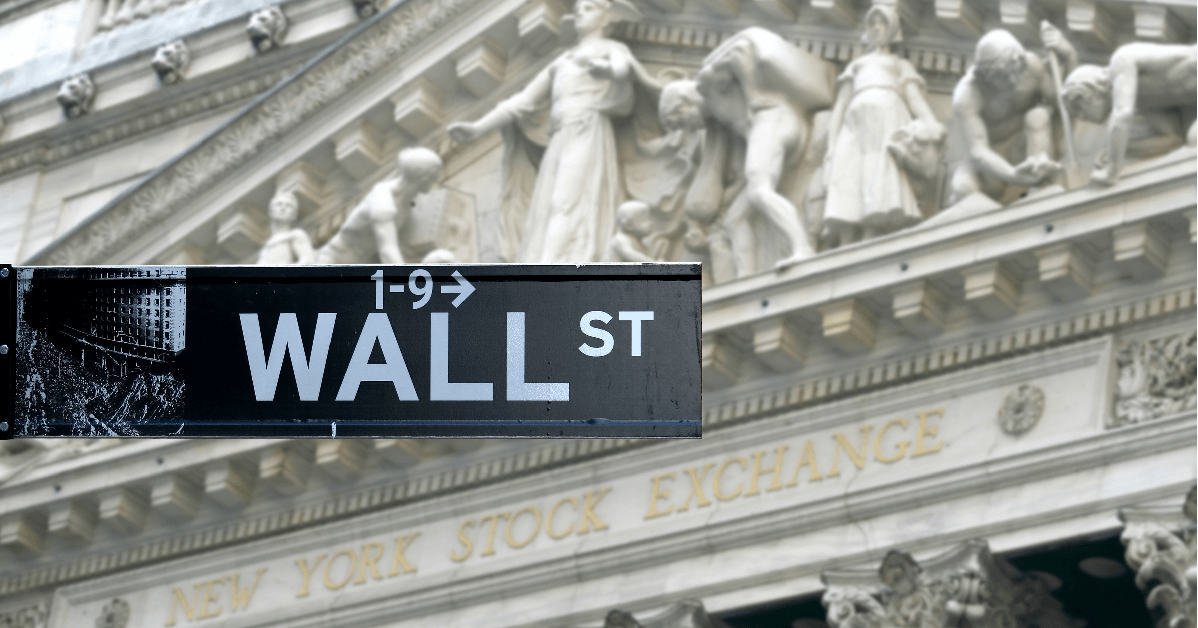 Close up image of a street sign reading "wall street" in front of the New York Stock Exchange building.