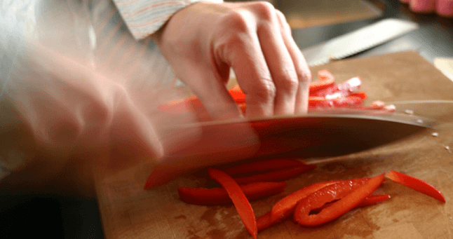 Close up image of hands chopping a red bell pepper.