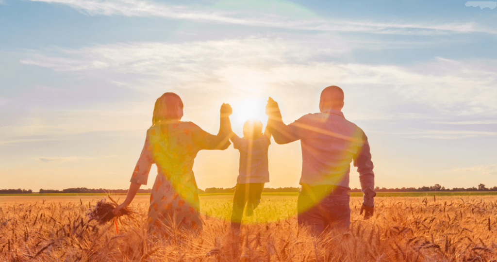 Two parents lifting their child between them during sunset in a field.