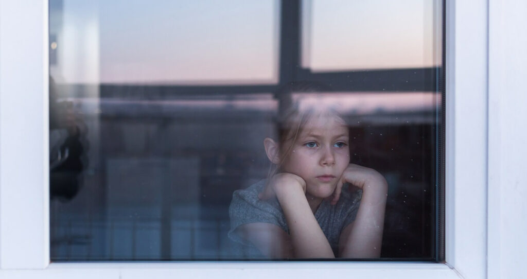 Young girl looking mournfully out of a window.