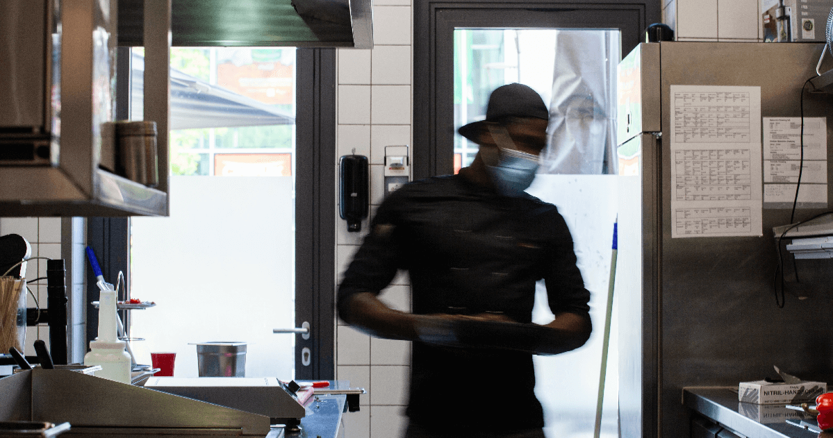 Image of a black worker in the back of a restaurant, wearing a mask.