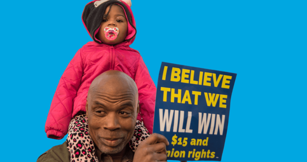 Father with daughter on his shoulders holding a Fight for $15 protest sign.