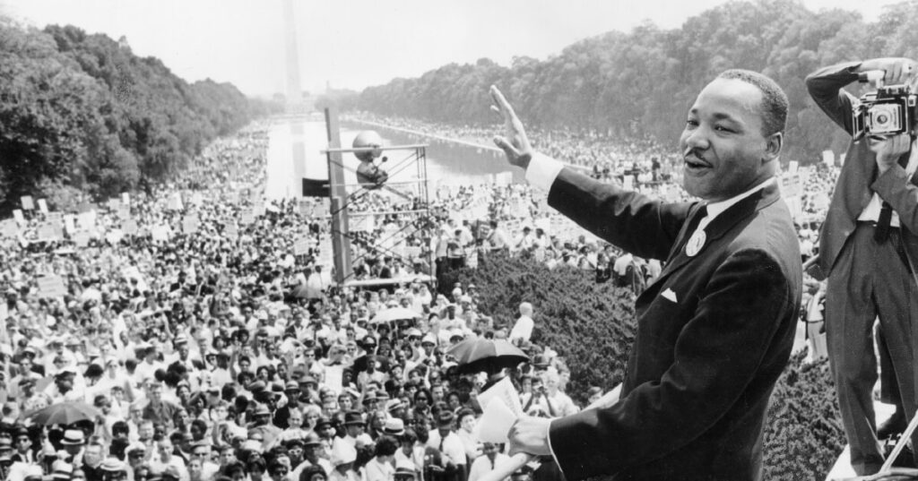 Black and white photo of MLK in front of the reflecting pool in DC giving his I Have a Dream speech.