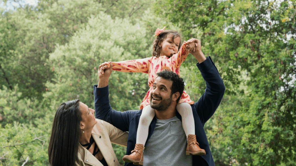 Family in a park with child on their father's shoulders