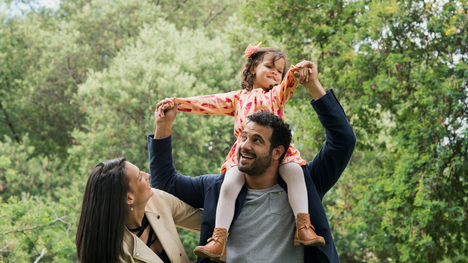 Family in a park with child on their father's shoulders
