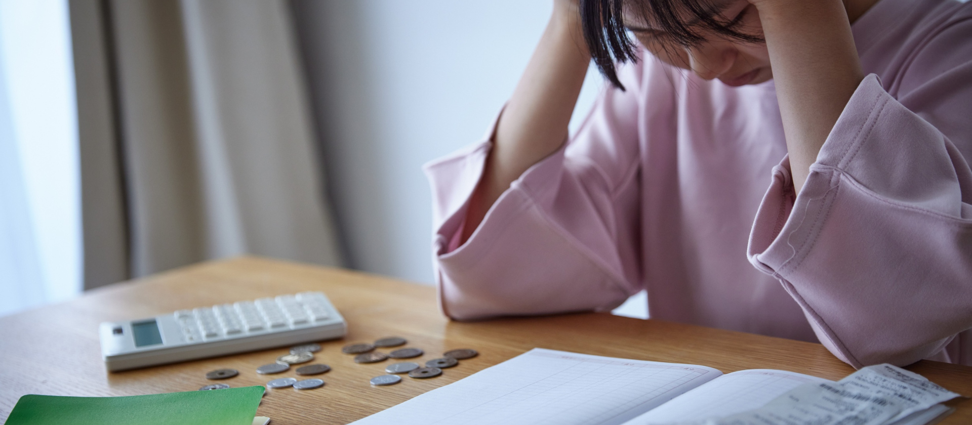 A person sits at their table with a calculator and receipts looking exhausted